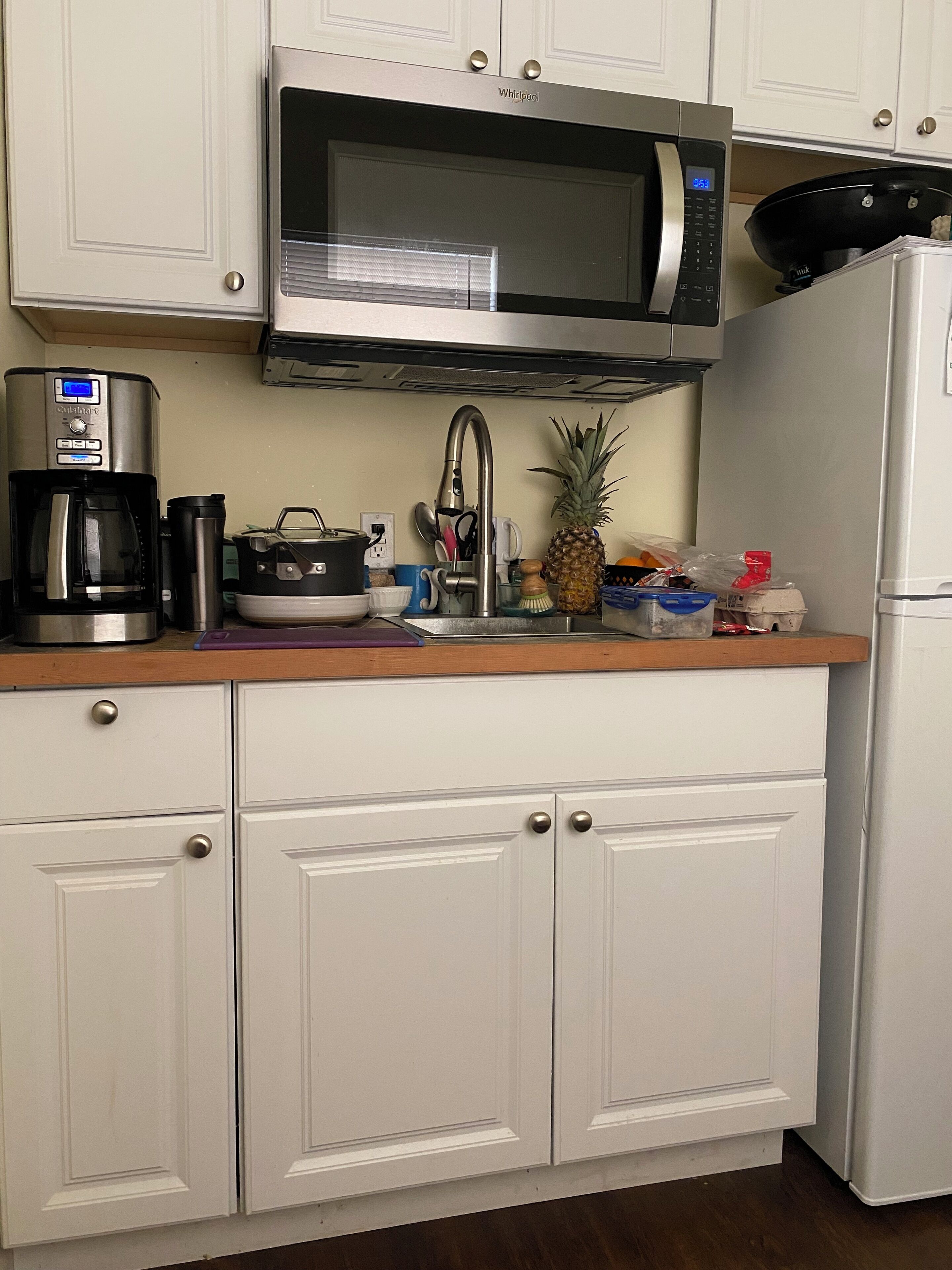 Eine Küche mit weißen Schränken, einer Edelstahl-Mikrowelle, einer Kaffeemaschine, einem Spülbecken und einem Kühlschrank.