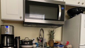 Eine Küche mit weißen Schränken, einer Edelstahl-Mikrowelle, einer Kaffeemaschine, einem Spülbecken und einem Kühlschrank.