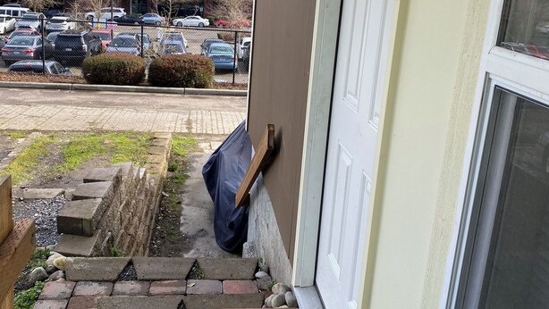 Ein Hauseingang mit einem Betonweg, der zu einer Tür führt, einer hölzernen Bank und einem geparkten Auto im Hintergrund.