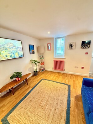 A spacious living room with a large painting, a potted plant, a blue sofa, and a wooden bench. - Stable Cottage – A Hidden Gem in Abergavenny Town (Abergavenny)