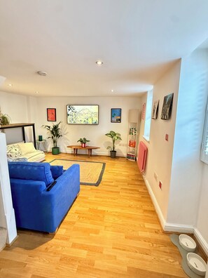 Uma sala de estar moderna com sofá azul, piso de madeira e área de jantar com mesa e cadeiras.