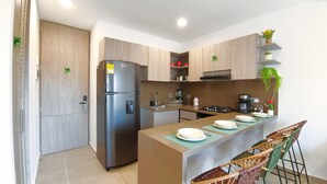 Una cocina moderna con refrigerador empotrado, estufa y pileta. Hay armarios de madera, una pequeña isla con platos y una silla.