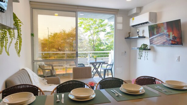 Un comedor con vistas al balcón, una mesa de comedor dispuesta con platos y cubiertos, y un sofá con una manta.