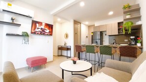 Una sala de estar moderna con una televisión de pantalla plana, una pequeña mesa de comedor y una zona de cocina con nevera y estufa.