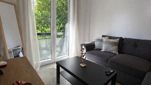 Un salon moderne avec un canapé gris, une table basse noire et une vue sur la verdure grâce à une porte-fenêtre coulissante.