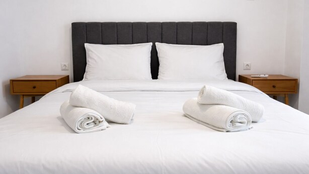Un lit bien fait, avec des draps blancs et deux serviettes enroulées posées sur le lit.