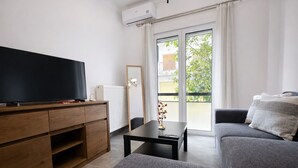 Un salon moderne avec un téléviseur à écran plat, des meubles en bois, un canapé et une table agrémentée d’un vase.