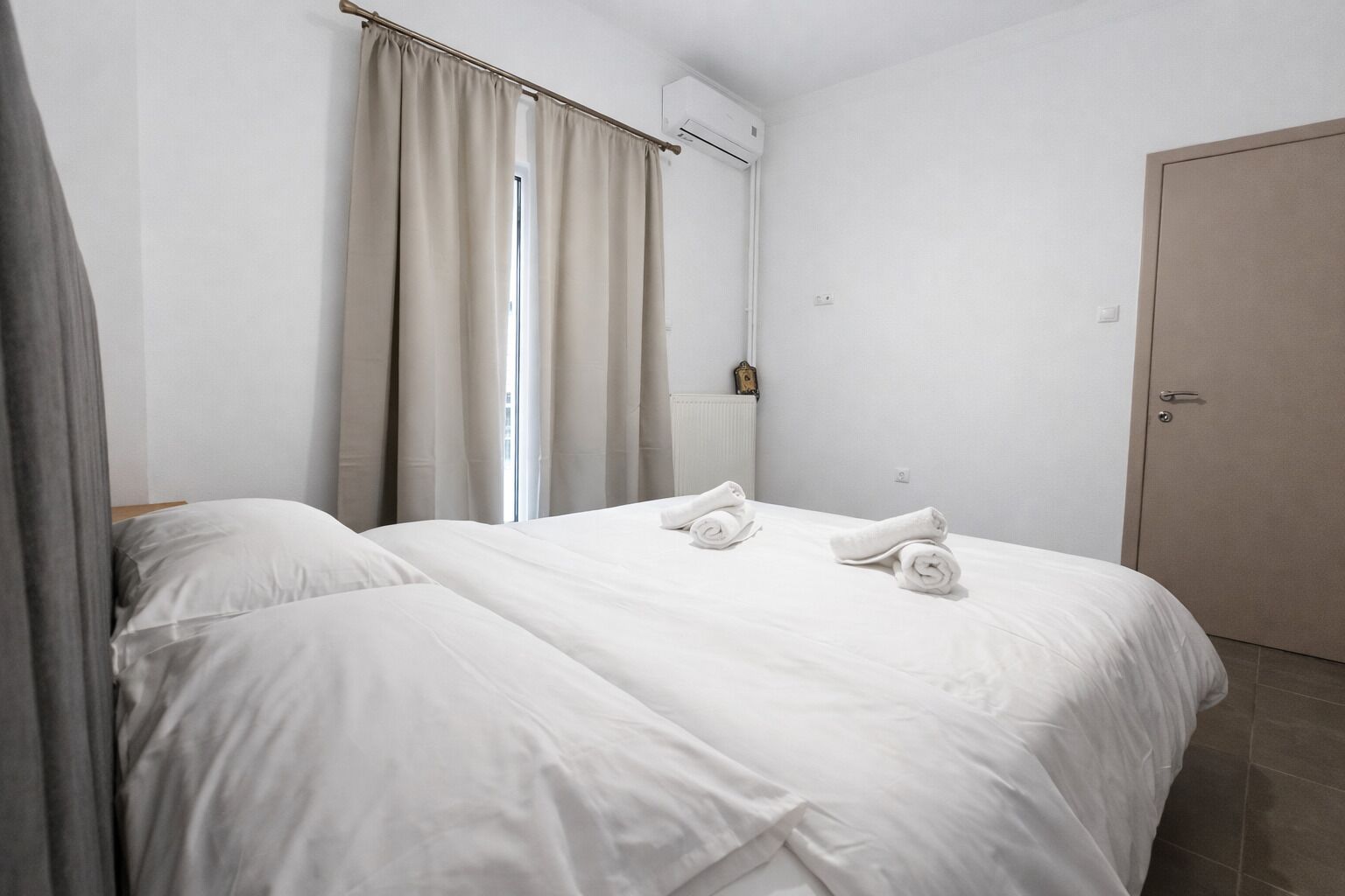 Een hotelkamer met twee bedden, een raam met gordijnen, een airconditioner en een deur.
