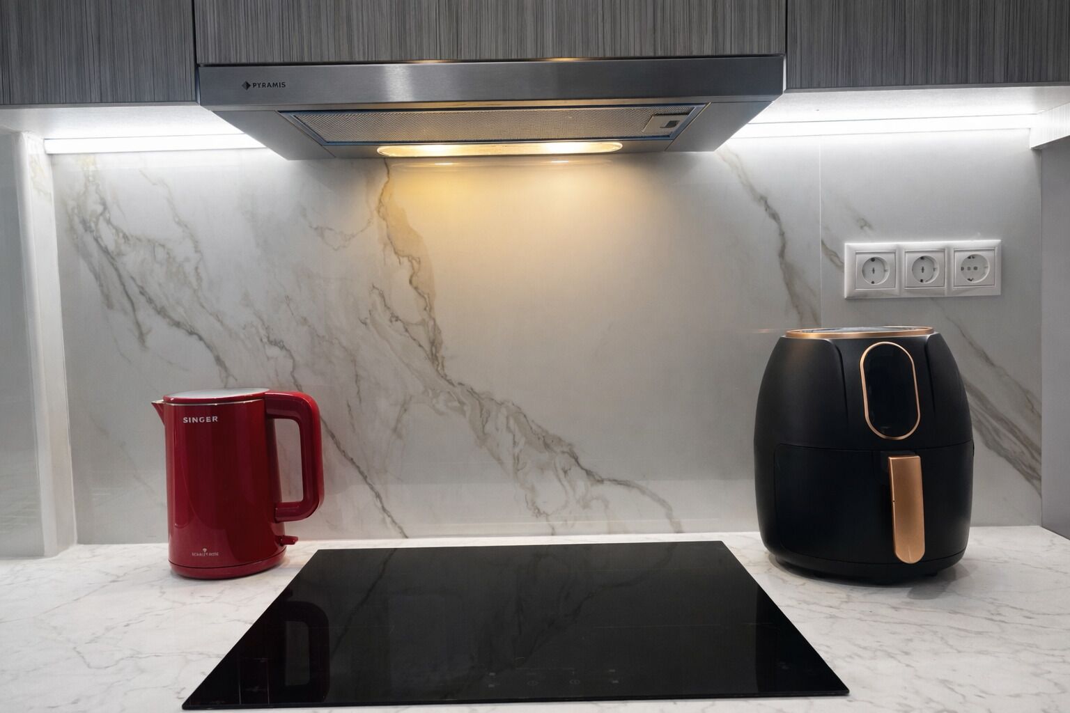 A modern kitchen with a built-in stove, a red kettle, and a black air fryer.