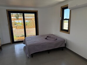 A bedroom with a bed, a window, and a sliding glass door leading to an outdoor area.