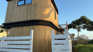 Une structure en forme de tour, faite de bois, avec un balcon, entourée d’une clôture blanche.