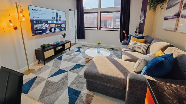 Een moderne woonkamer met een bank, salontafel en een tv met een ingebouwd scherm waarop een videogesprek wordt weergegeven.