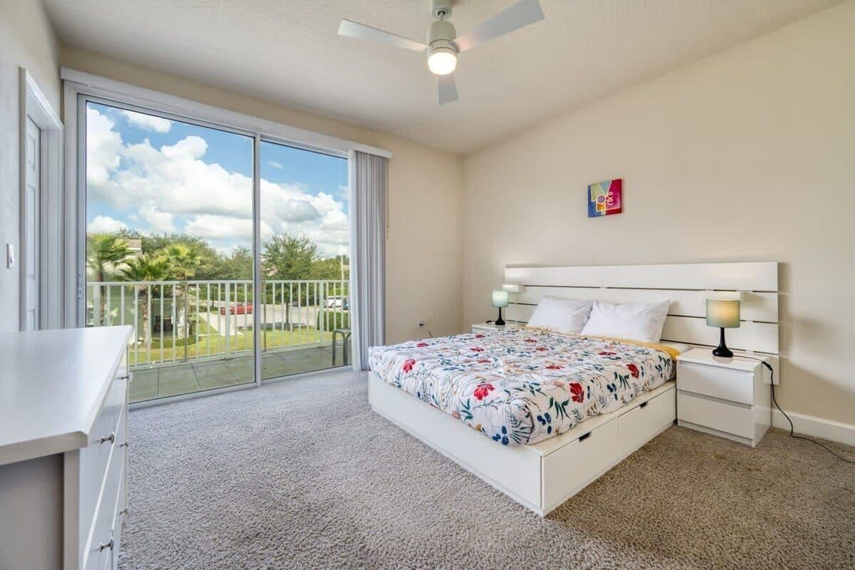 A bedroom with a bed, bedside tables, a ceiling fan, and a view of the outdoors through a sliding glass door.