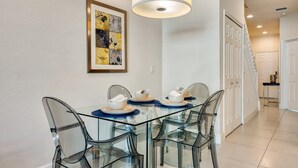 Een moderne eethoek met een glazen tafel en stoelen, een ingelijste afbeelding aan de muur en een trap op de achtergrond.