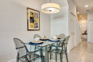 A modern dining area with a glass table and chairs, a framed artwork on the wall, and a staircase in the background. - 3BR Home w/ Private Pool Near Disney (Clermont)