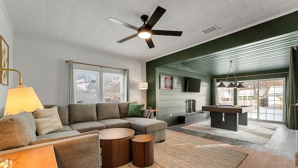 A modern living room with a sectional sofa, two round wooden side tables, a ceiling fan, and a large window with blinds. - Spacious 3BR Home Near Burlington with hot tub ~ Sleeps 12 (Winooski)