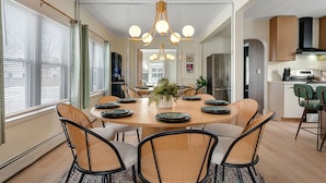 A modern dining area with a round table, wicker chairs, and a central plant. - Spacious 3BR Home Near Burlington with hot tub ~ Sleeps 12 (Winooski)