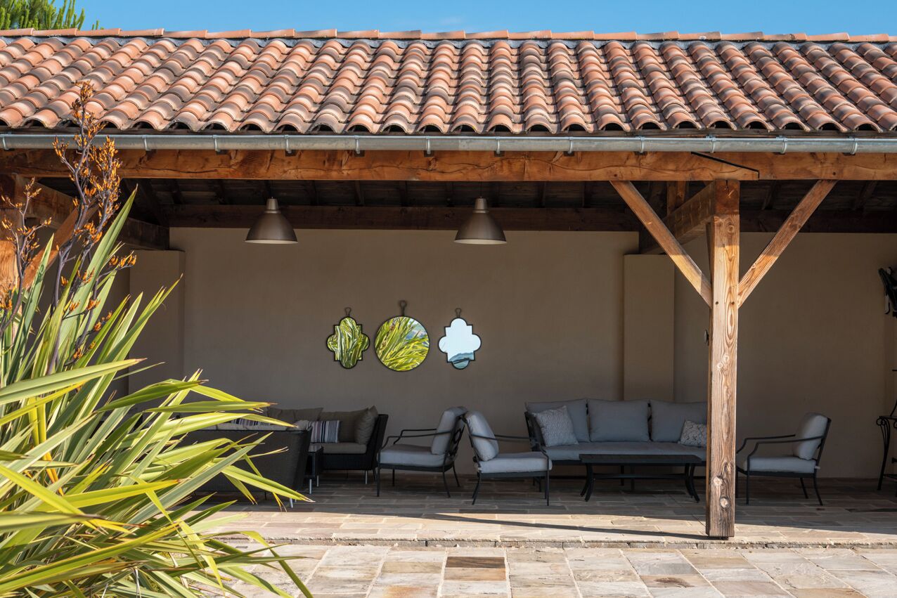 An outdoor patio area with a tiled roof, wooden pergola, and seating arrangements.