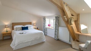 A bedroom with a wooden ceiling, a bed with white bedding, a bedside table with a lamp, a window with curtains, and a bedside mirror.