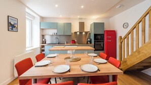 Une cuisine moderne avec des meubles de couleur turquoise, une table à manger en bois pour six personnes et un réfrigérateur rouge.