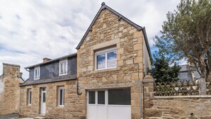 Une maison en pierre avec un garage, un petit porche et une clôture en bois.