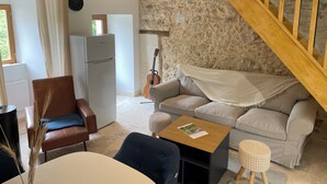 Een gezellige woonkamer met een stenen muur, een houten trap, een bank, een stoel, een tafel en een gitaar die tegen de muur staat.