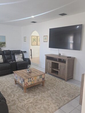 Ein Wohnzimmer mit einer schwarzen Ledersofa, einem Couchtisch mit bunten Fliesen, einem Fernsehgerät an der Wand und einem Holzschrank.