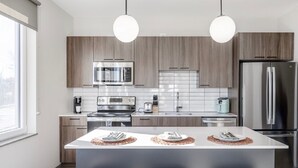 A modern kitchen with wooden cabinets, stainless steel appliances, and pendant lighting. - Elysian Residences Boston (Boston)