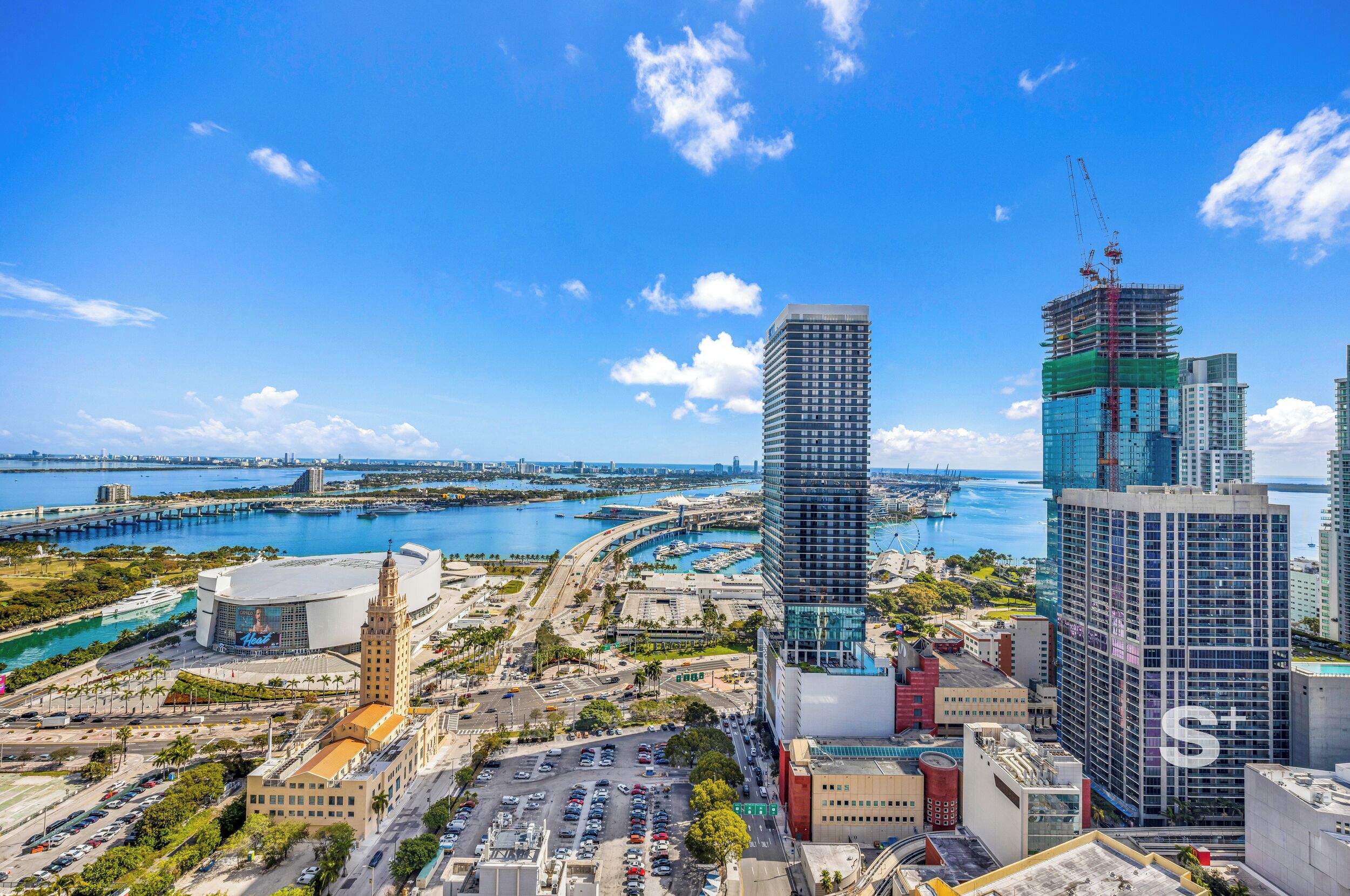 A cityscape with a prominent building under construction, a marina, and a large stadium.