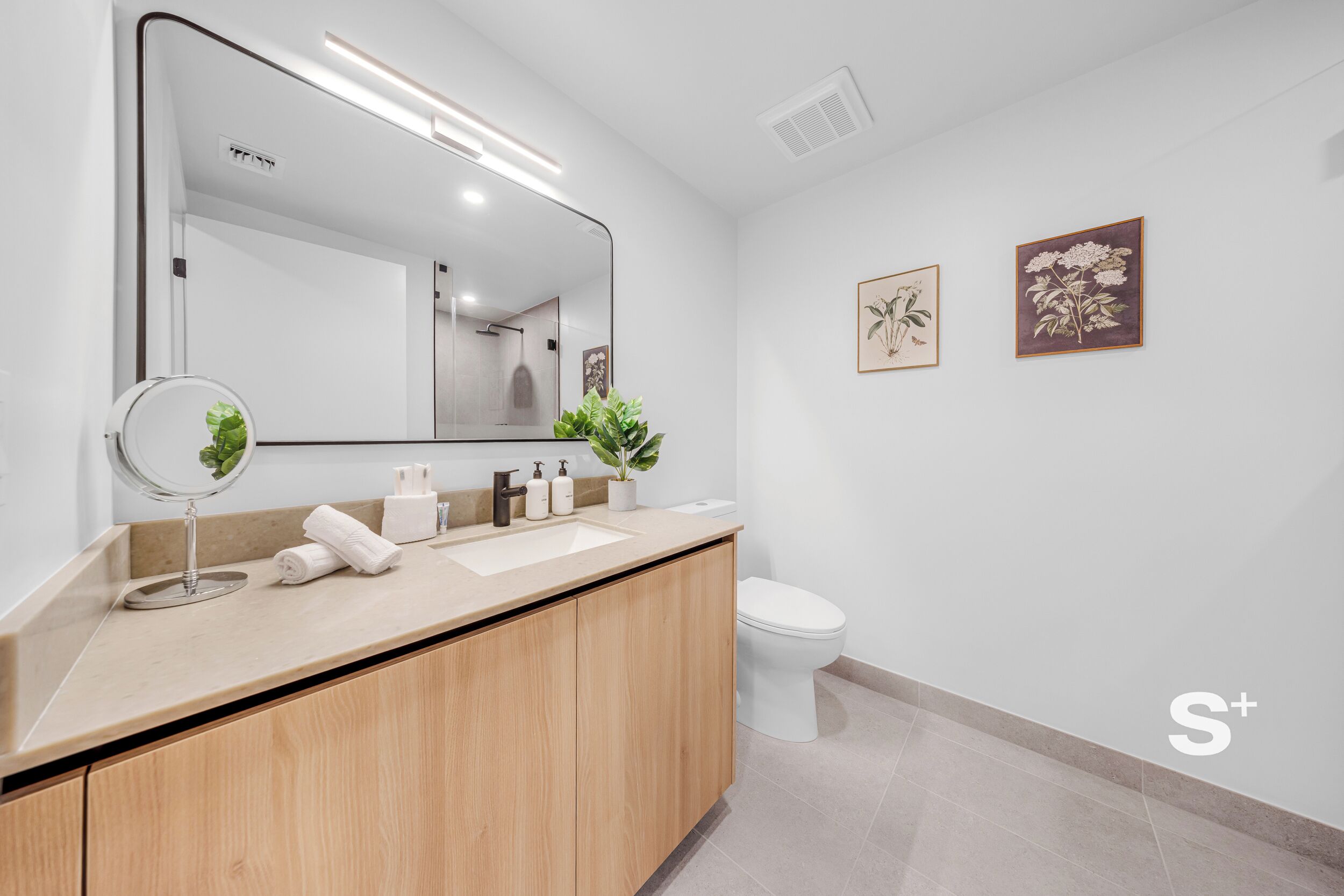 Une salle de bain moderne avec un grand miroir, un lavabo équipé de produits de toilette et des toilettes.