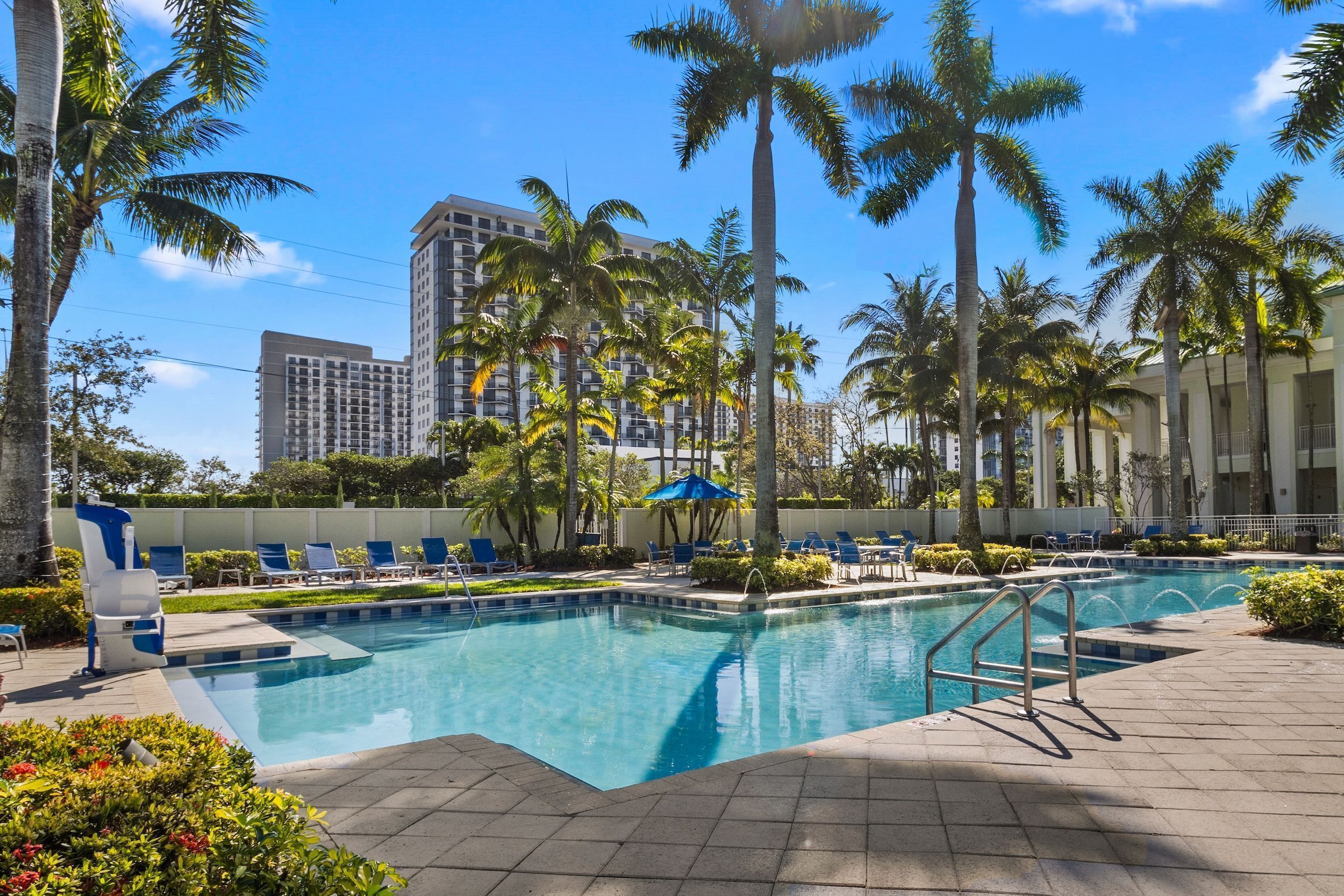 A swimming pool with lounge chairs, palm trees, and a building in the background.