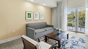 A living room with a grey sofa, a wooden coffee table, and a patterned rug. There are three framed pictures on the wall. - 1BR Double Suite w/ Kitchen | Pool & Restaurant (Miami)
