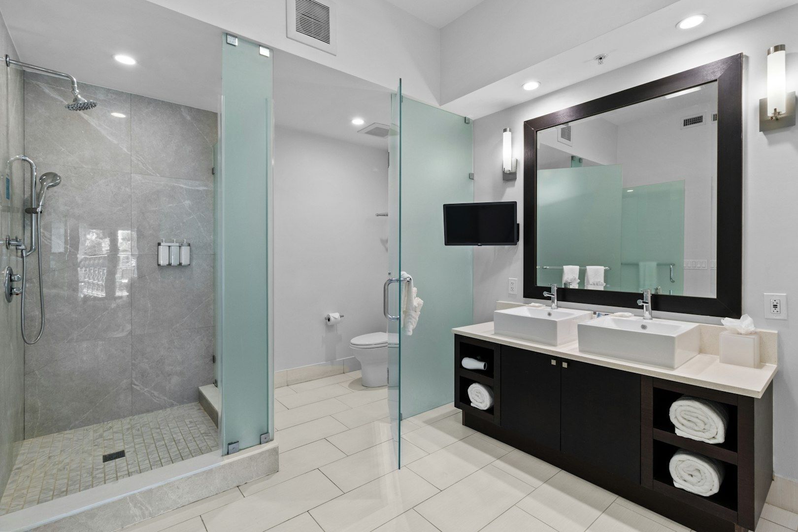 A modern bathroom with a glass-enclosed shower, a vanity with dual sinks, and a large mirror.
