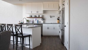 A kitchen with white cabinets, a central island with bar stools, a refrigerator, and a sink. - Spacious and fully loaded 4 Bed 4 Bath with Amazing Views on Grand Lake. (Afton)