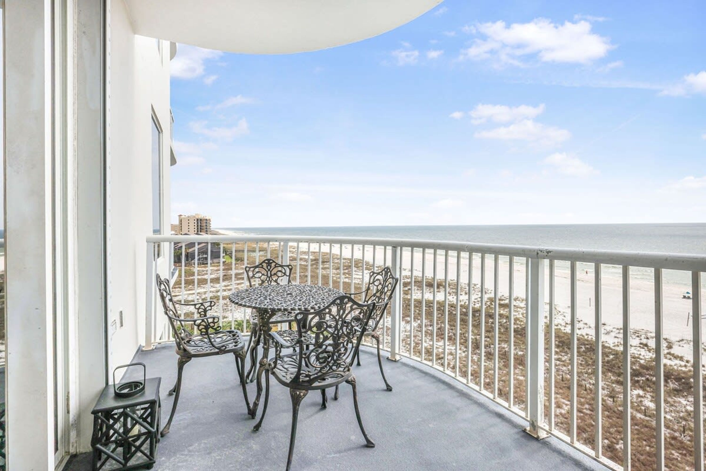 Een balkon met een ronde tafel en stoelen, met uitzicht op een strand.