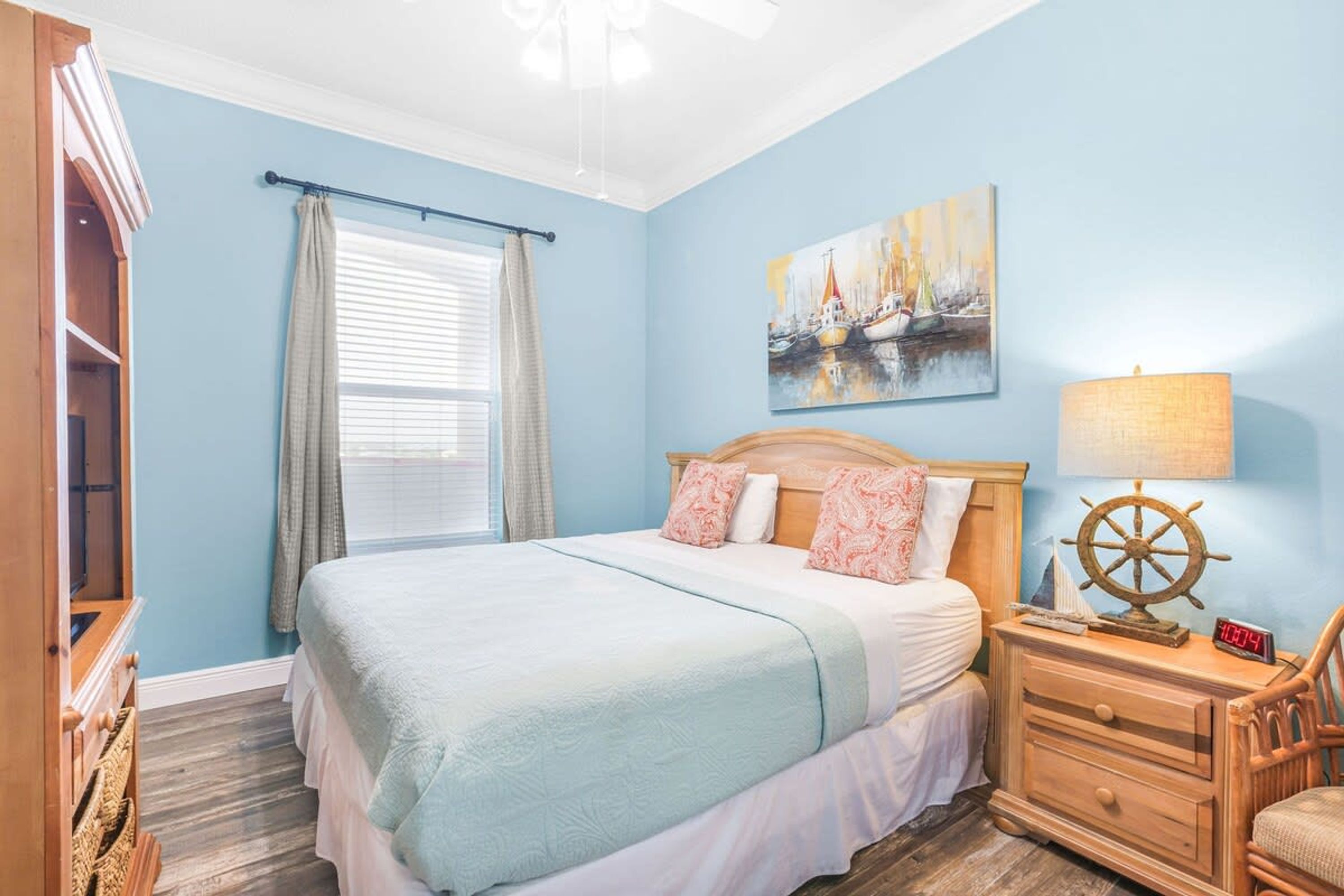 A bedroom with a bed, a nightstand, a chair, a window with curtains, and a painting on the wall.