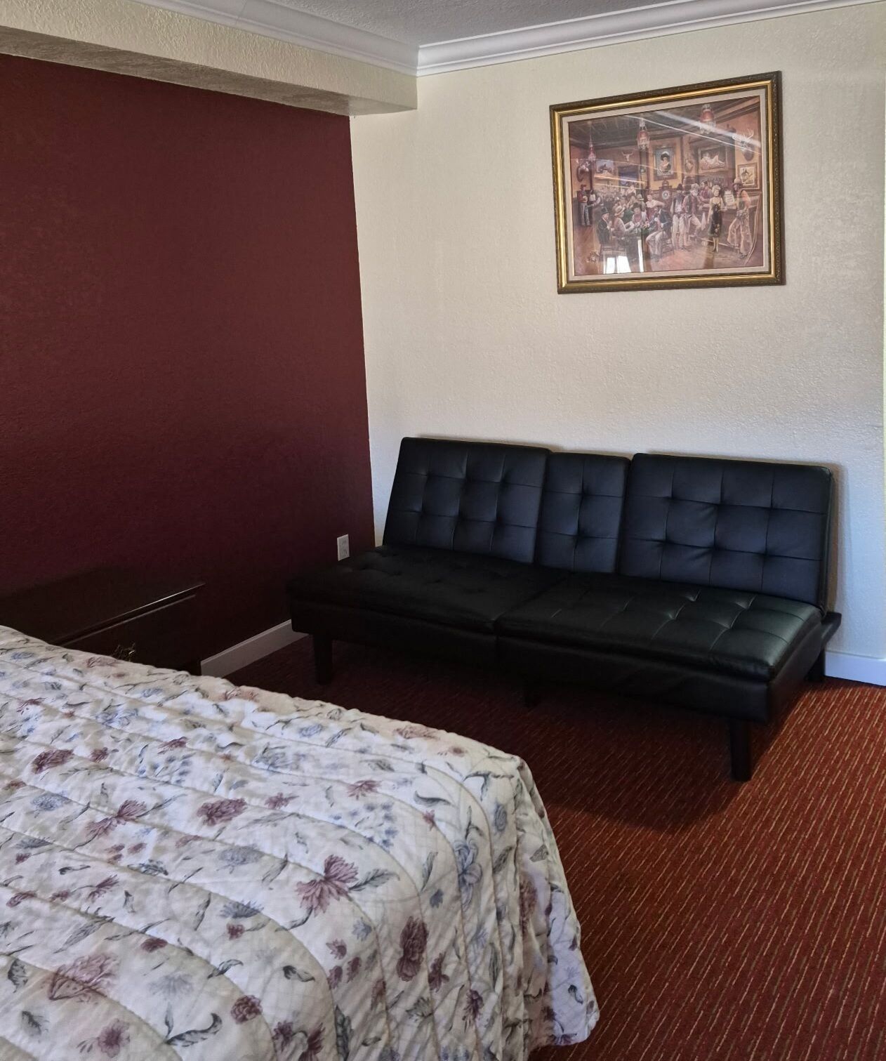 A hotel room with a bed, a sofa, a framed picture on the wall, and a carpeted floor.