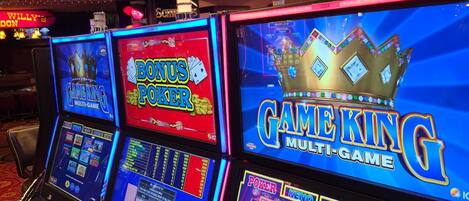 Un área de juegos con varias máquinas tragamonedas y una pantalla grande que muestra un juego llamado "Game King Multi-Game".