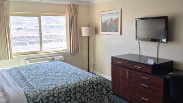 A hotel room with a bed, a desk, a chair, a TV, and a window with curtains.