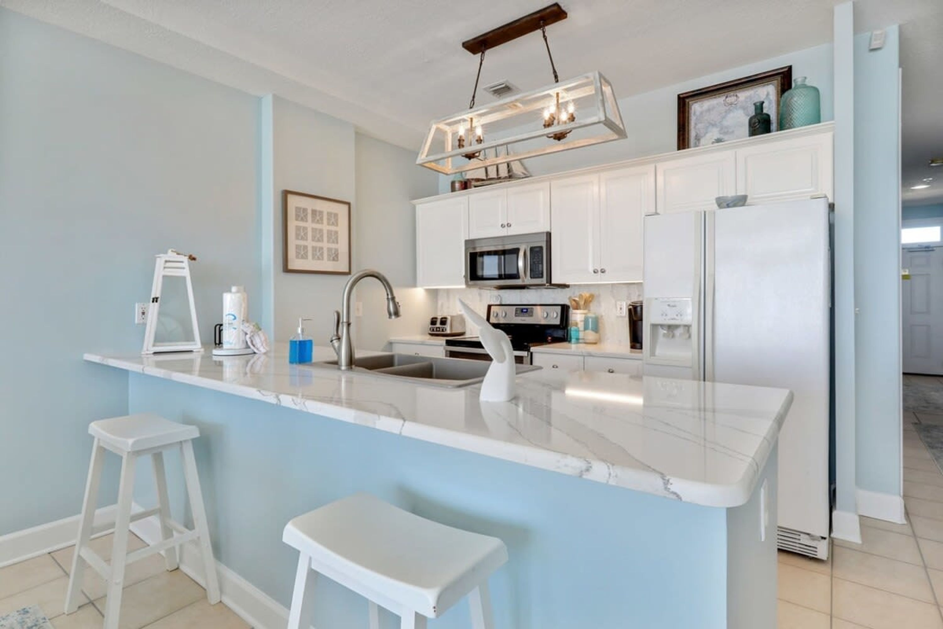 A modern kitchen with white cabinetry, a marble island, and a hanging light fixture.