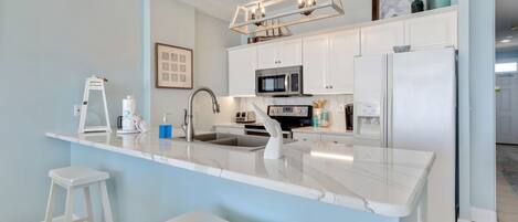 A modern kitchen with white cabinetry, a marble island, and a hanging light fixture.