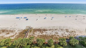 A beach with umbrellas, a lifeguard tower, and palm trees. - Regency Isle 1104 Penthouse With 3 Bedrooms (Orange Beach)