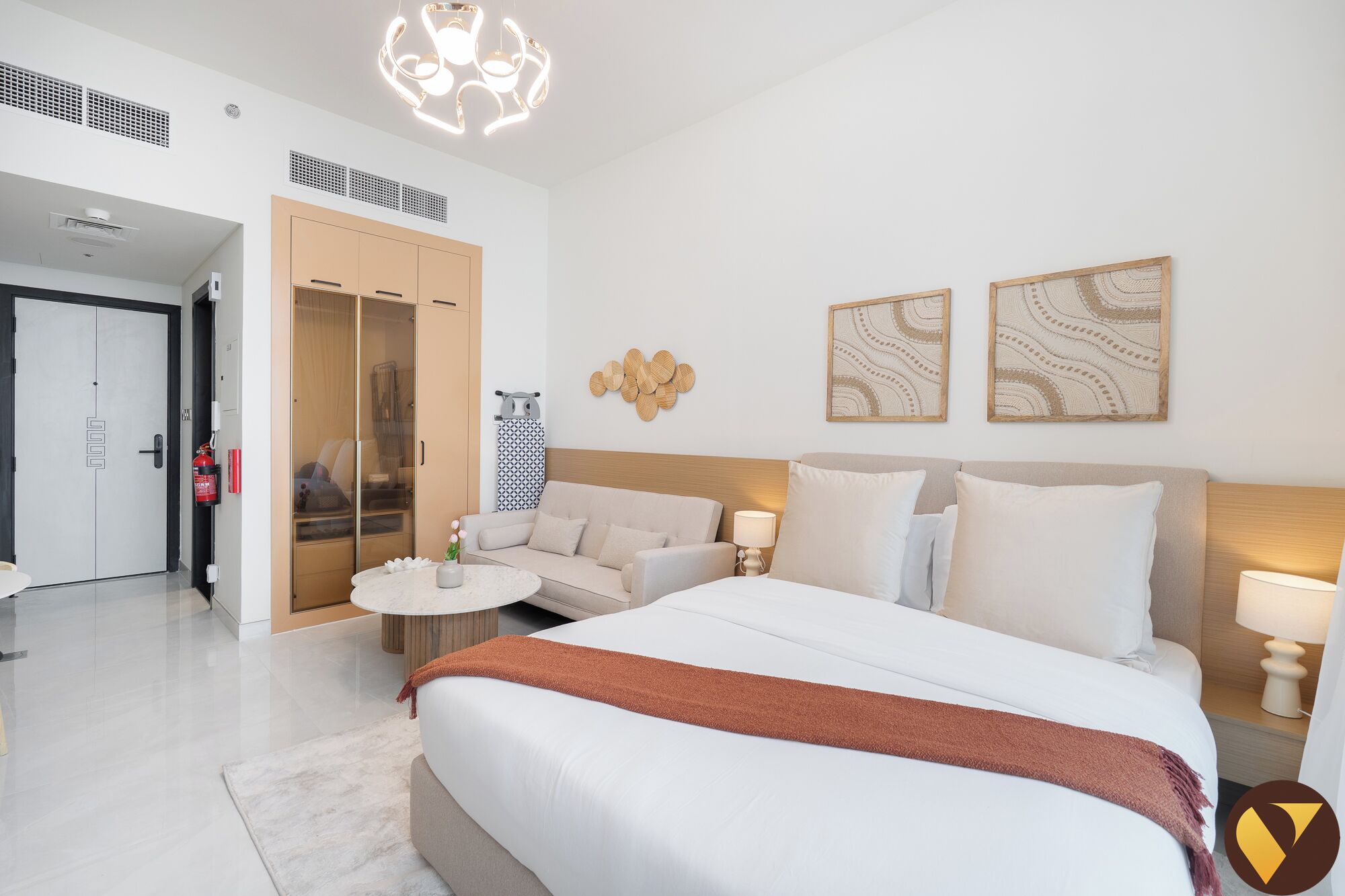 A modern hotel room with a large bed, a sofa, a small round table, and a ceiling light fixture.
