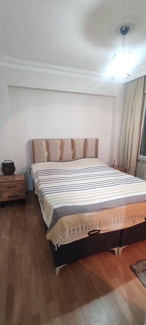 A bedroom with a bed, wooden nightstand, and a ceiling light.