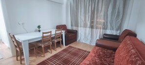 A dining area with a white table and wooden chairs, a brown sofa, and a patterned rug.
