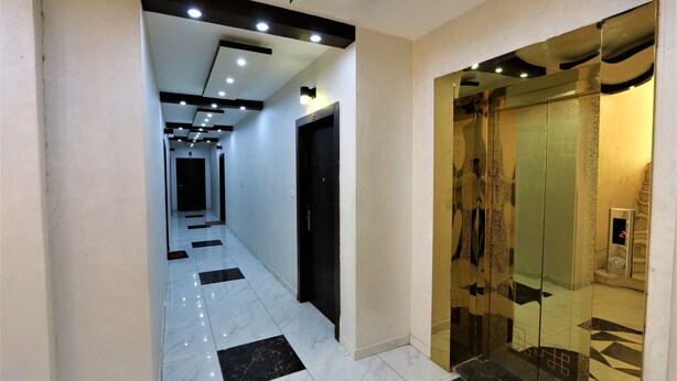 A hallway with a modern design, featuring a checkered floor pattern, recessed ceiling lighting, and a glass elevator with a digital display. - 7th Circle Diamnod (Amman)