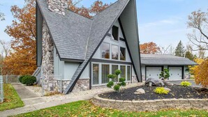 Uma casa moderna com fachada de pedra, telhado inclinado e um jardim frontal ajardinado com uma pequena árvore e pedras.