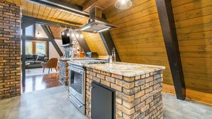 Cozinha com ilha de tijolos, eletrodomésticos de aço inoxidável e luminária pendente.
