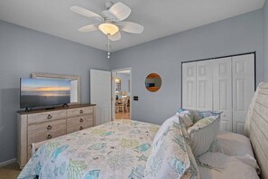 A bedroom with a bed, a TV, a dresser, a ceiling fan, and a door. - Sunset Beach Escape! (Sunset Beach)