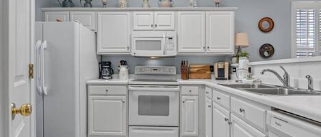 A kitchen with white cabinets, a refrigerator, a microwave, an oven, and a sink.